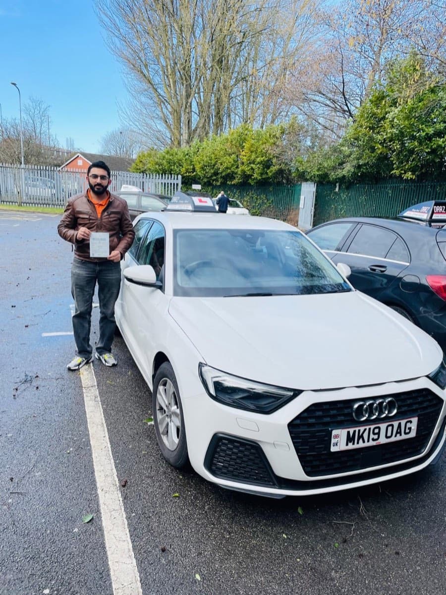 Wearing a brown leather jacket and glasses, a learner presents a pass certificate by the white Audi under a crisp blue winter sky.