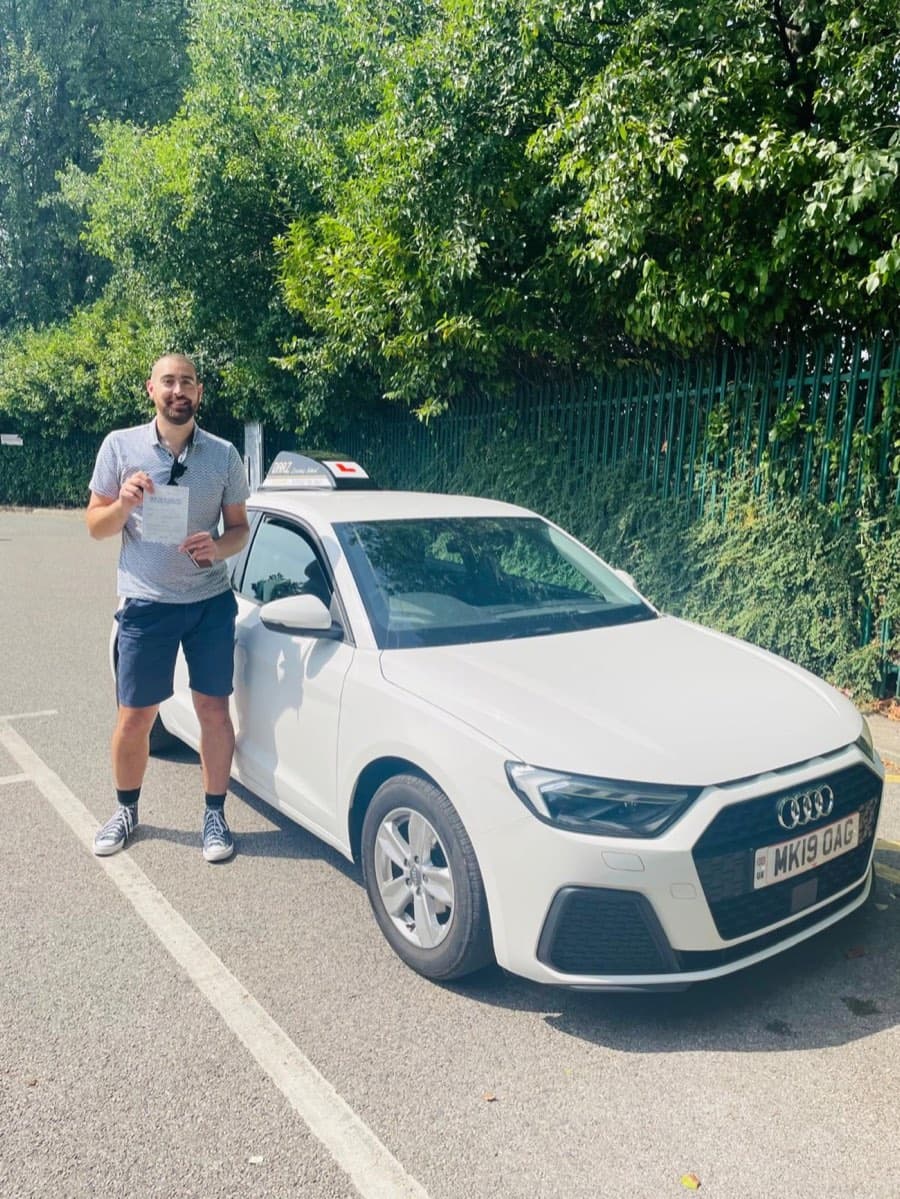Bright summer sunshine as a learner in a grey polo and navy shorts shows a certificate by the tuition car.