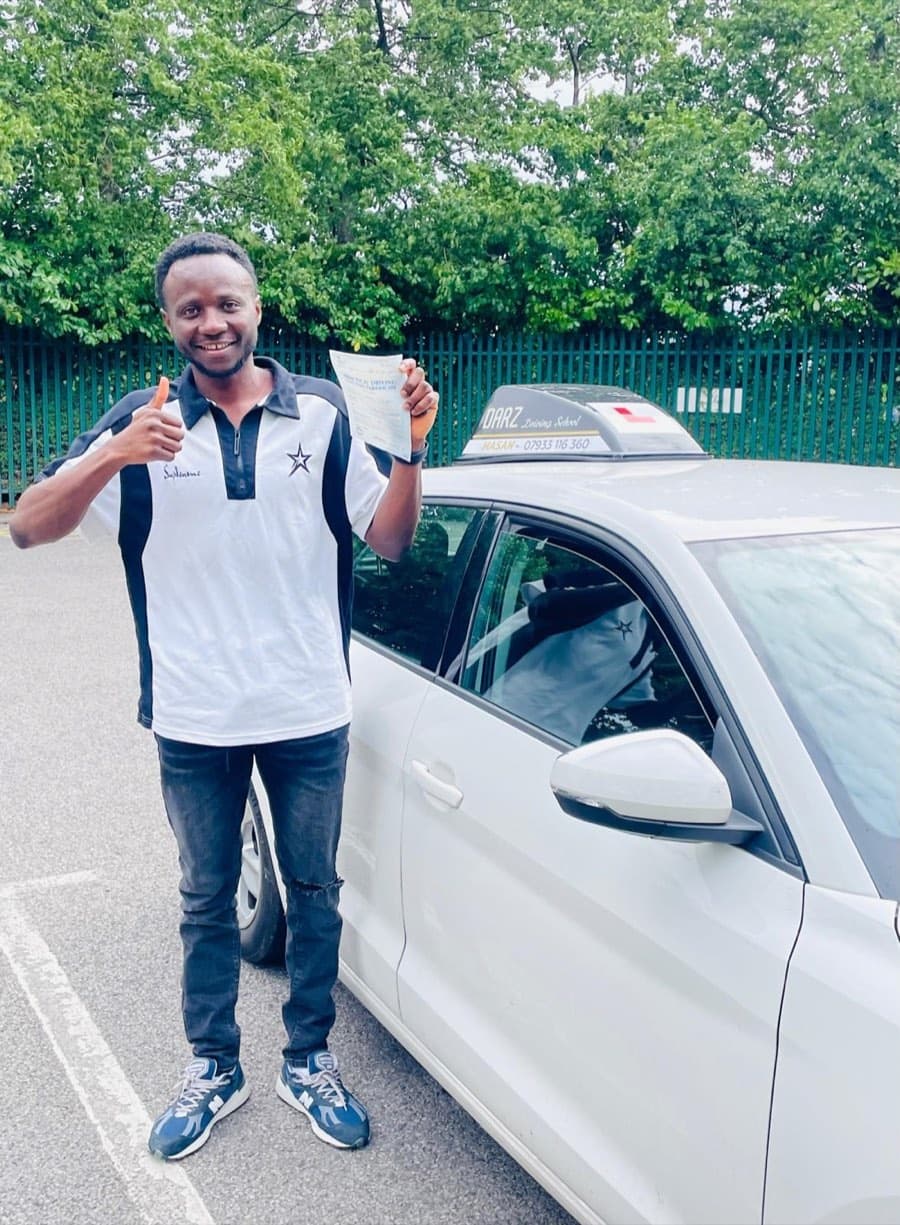 Thumbs up from a learner in a black and white polo shirt and jeans, certificate raised beside the tuition car.
