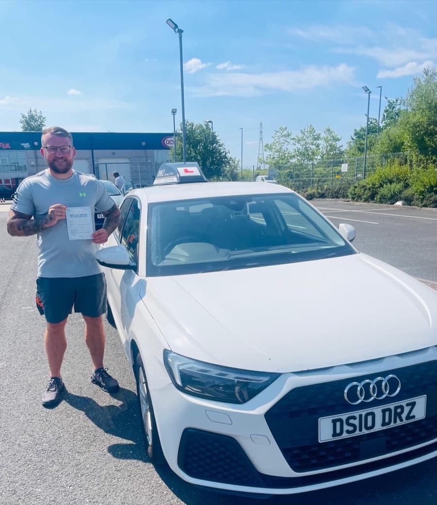 Bright sunshine over an industrial estate car park as a learner in a grey sports top and shorts displays a certificate.