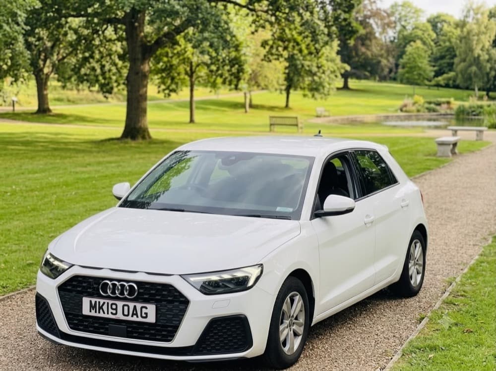 The white Audi A1 used for Magic Wheels driving lessons, parked on a tree-lined path.